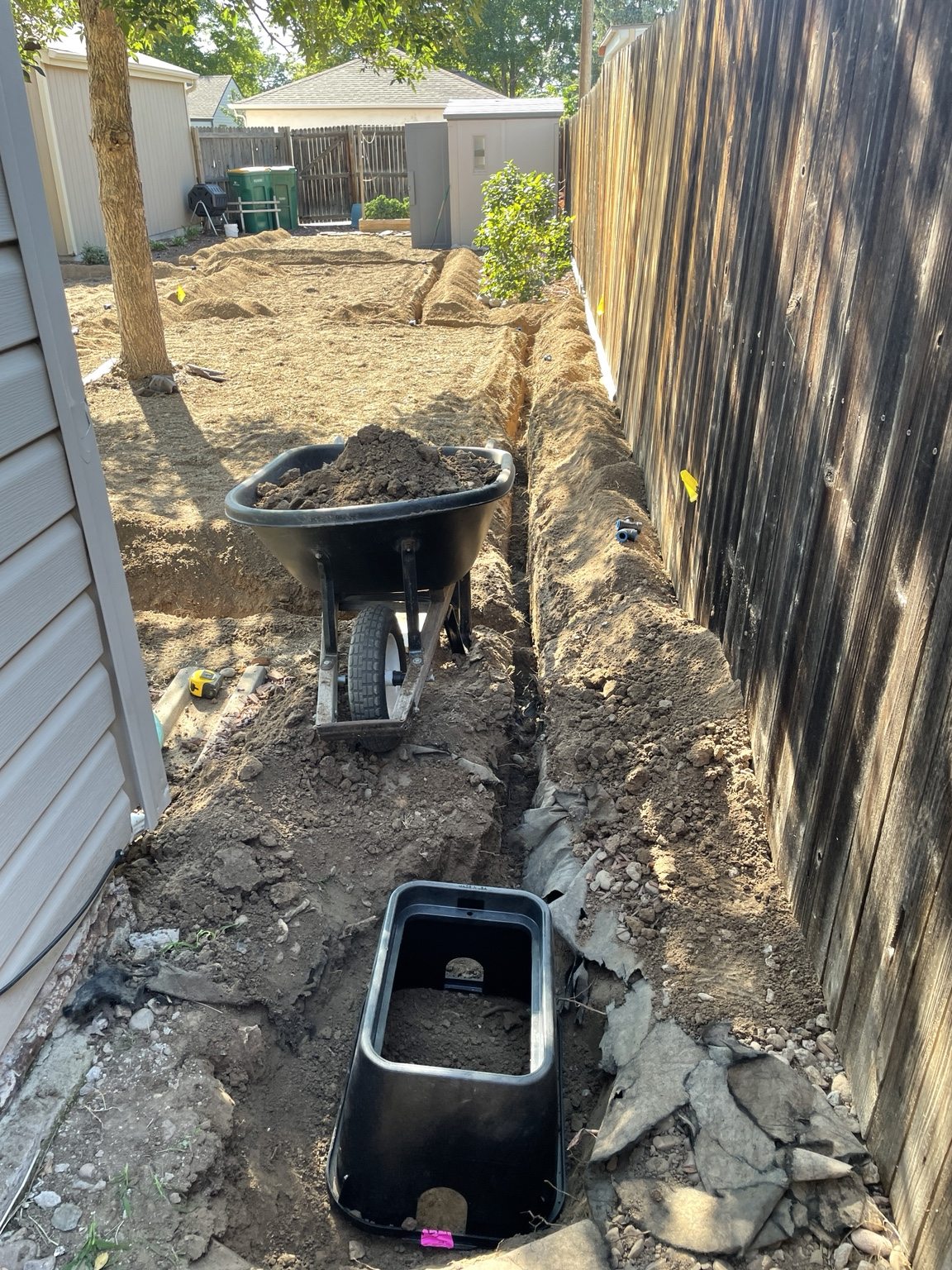 An excavated valve box with a wheelbarrow of soil beside it